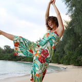 Femme en robe fleurie colorée posant sur une plage avec des arbres en arrière-plan