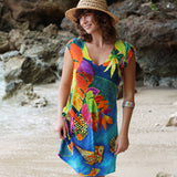 Woman wearing a colorful dress with fish patterns on a beach.
