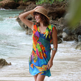 Une femme en robe colorée et chapeau de paille se tient au bord d'une rivière avec des rochers et de l'eau.