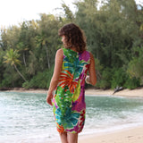 Woman in a colorful tie-dye dress standing on a beach with greenery in the background