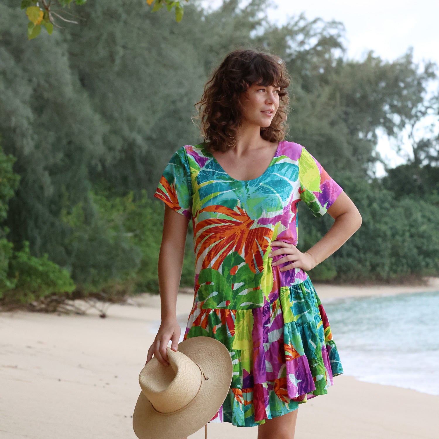 Woman in a colorful dress standing on a beach with trees in the background