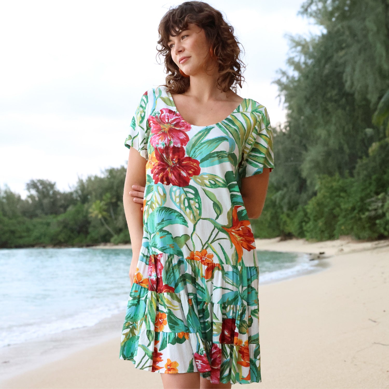 Woman wearing a floral dress on a beach with trees in the background