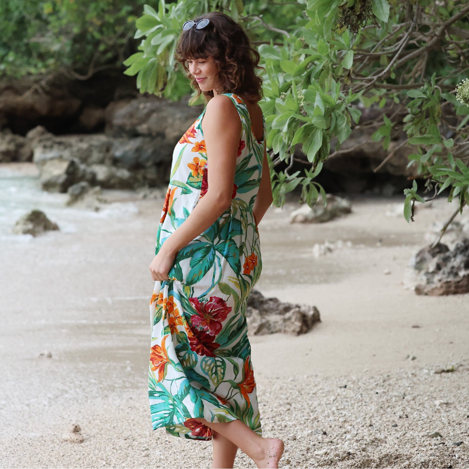 Woman in a floral dress standing on a beach with greenery in the background
