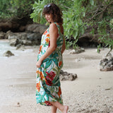 Woman in a floral dress standing on a beach with greenery in the background