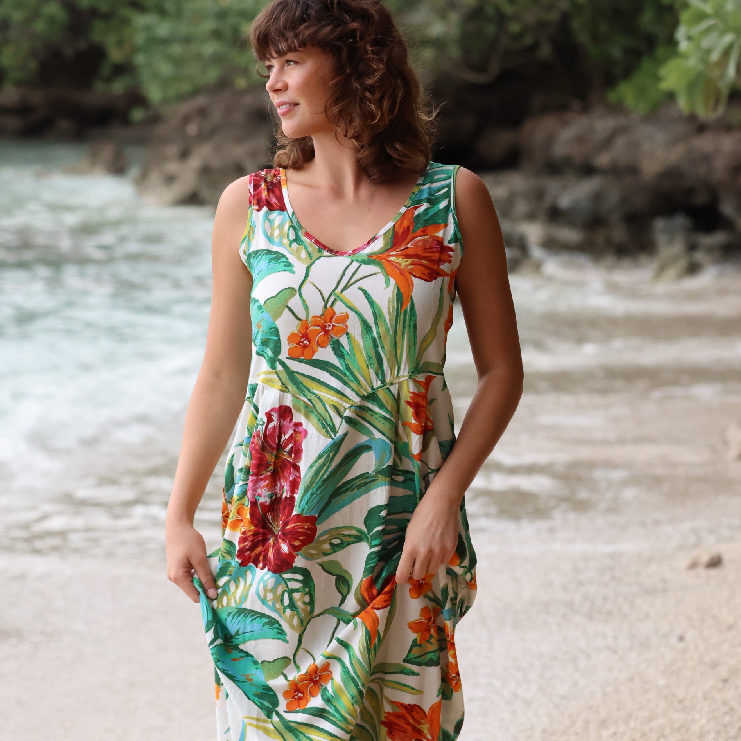 Woman wearing a colorful floral dress standing on a beach.