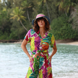 Woman in a colorful dress and hat standing by a body of water with greenery in the background