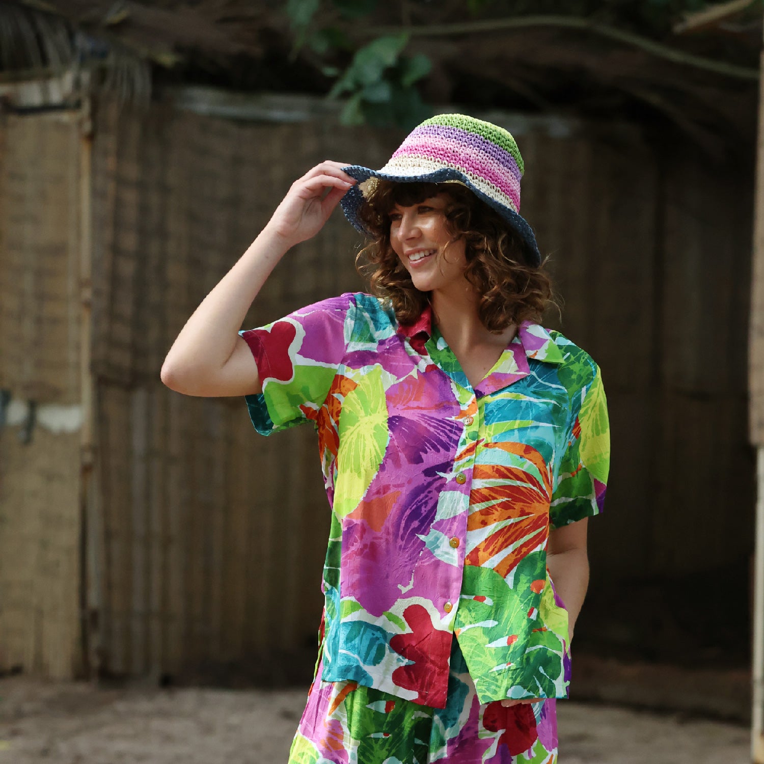 Person wearing a colorful shirt and hat, standing in front of a rustic wooden wall.