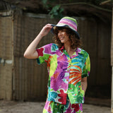 Person wearing a colorful shirt and hat, standing in front of a rustic wooden wall.