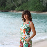 Femme en robe à fleurs debout sur une plage avec l'océan et la verdure en arrière-plan