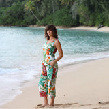 Woman in a floral dress standing on a beach with ocean and trees in the background