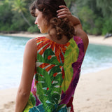 Woman in a colorful dress with a tropical leaf pattern standing on a beach.