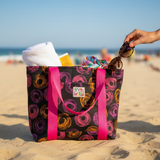 Beach bag with pink handles filled with beach items on a sandy beach.