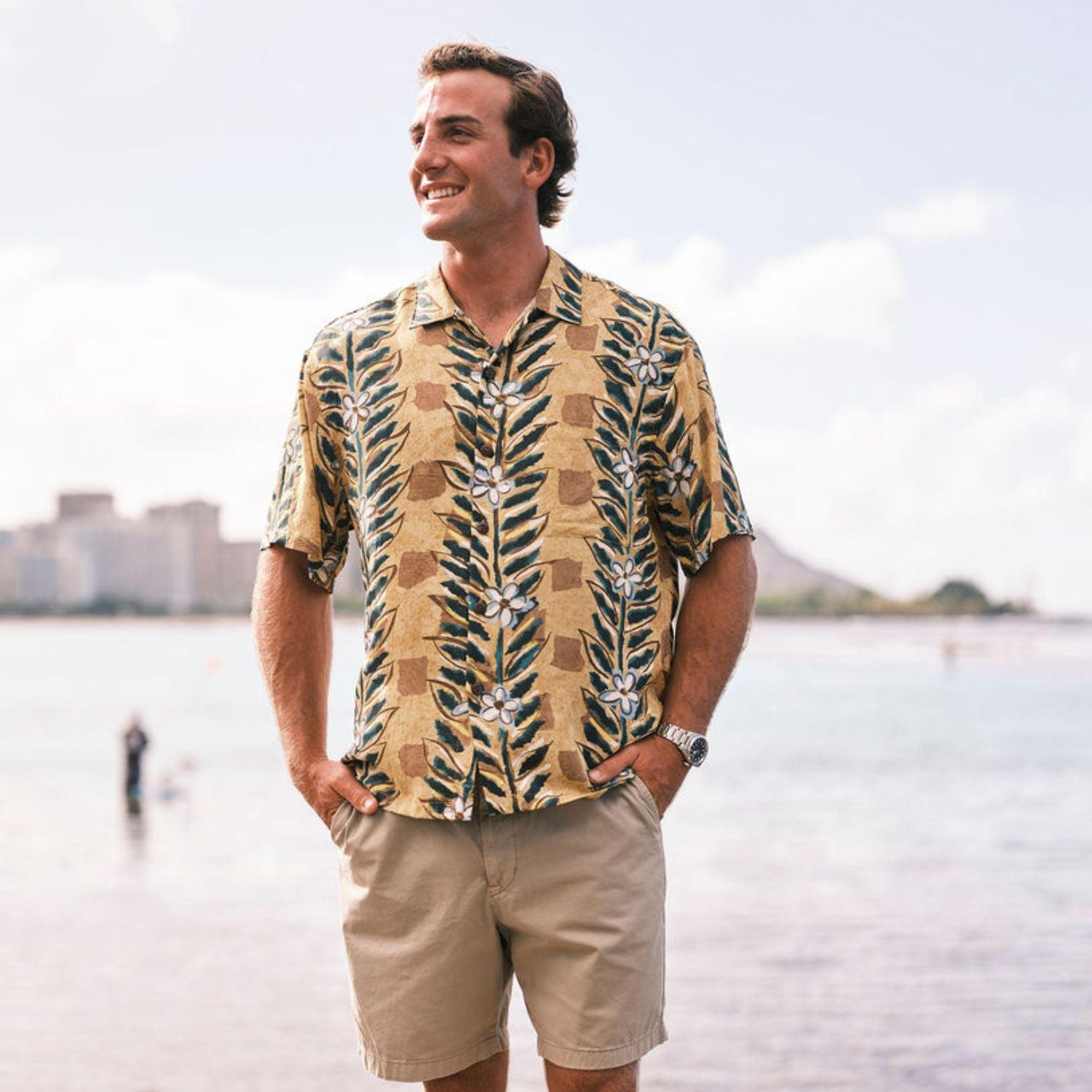 Man wearing a patterned shirt and shorts standing by a waterfront.