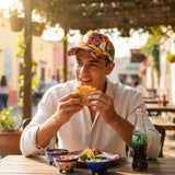 Man eating a taco outdoors with a bottle of soda and food on the table.