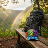 Backpack and colorful cap on a bench with a rainbow in the background