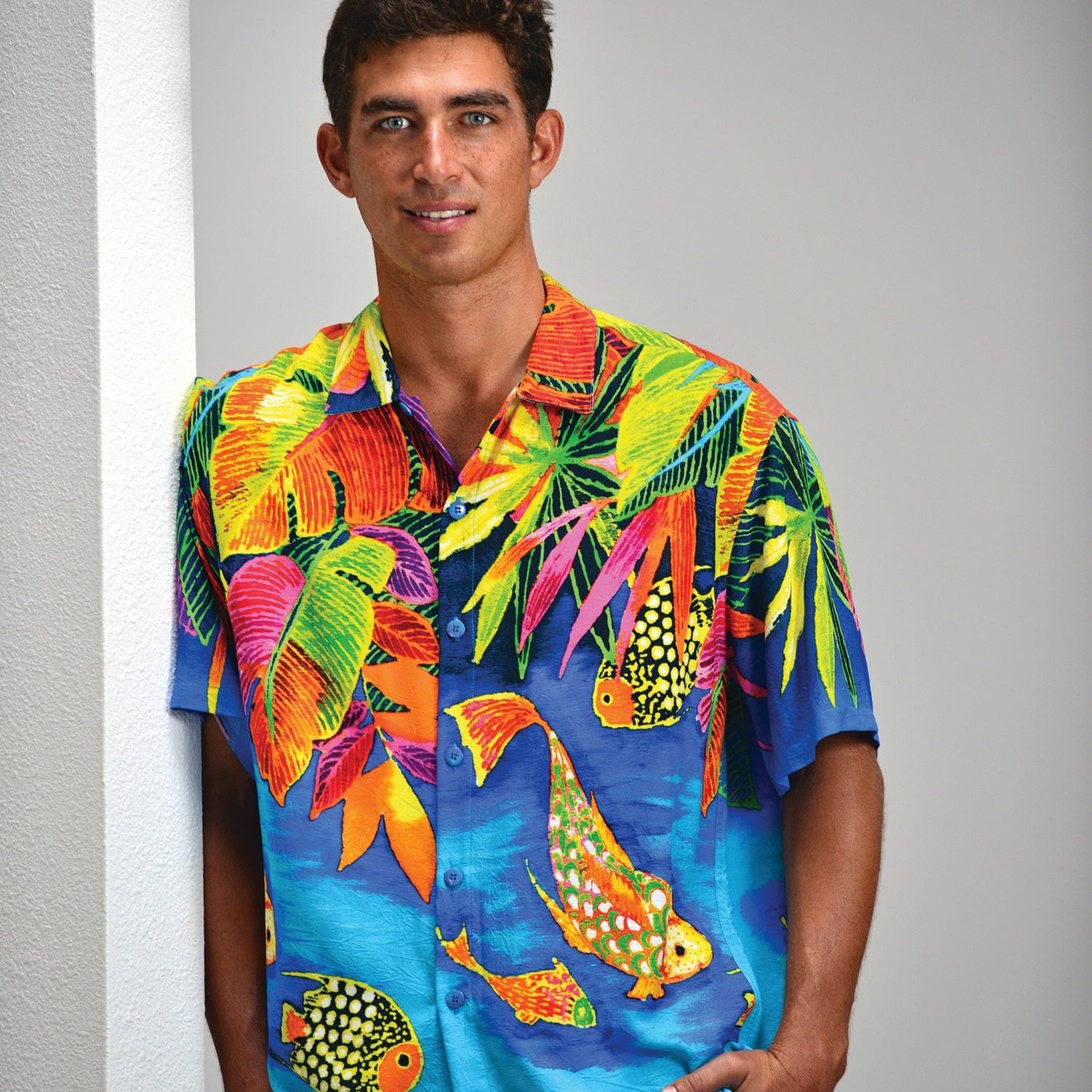 Man wearing a colorful tropical shirt with fish and leaf patterns against a plain background