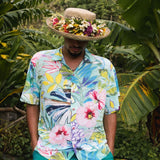 Man wearing a colorful floral shirt and hat with flowers in a tropical setting