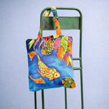 Colorful tote bag with fish design on a green chair against a light blue background