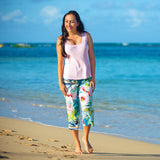 Woman standing on a beach wearing a pink top and colorful floral pants.