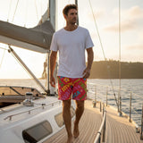 Man on a sailboat wearing colorful swim shorts and a white t-shirt.