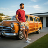 Man leaning against a vintage orange car with a wooden panel design, wearing a red shirt and colorful shorts.