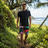 Man walking on a trail with ocean view wearing a black t-shirt and colorful shorts.