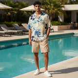 Man in a floral shirt and beige shorts standing by a poolside.