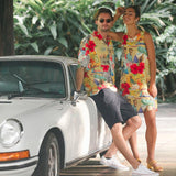 Un hombre y una mujer con atuendos coloridos a juego posan junto a un coche antiguo en un entorno tropical.