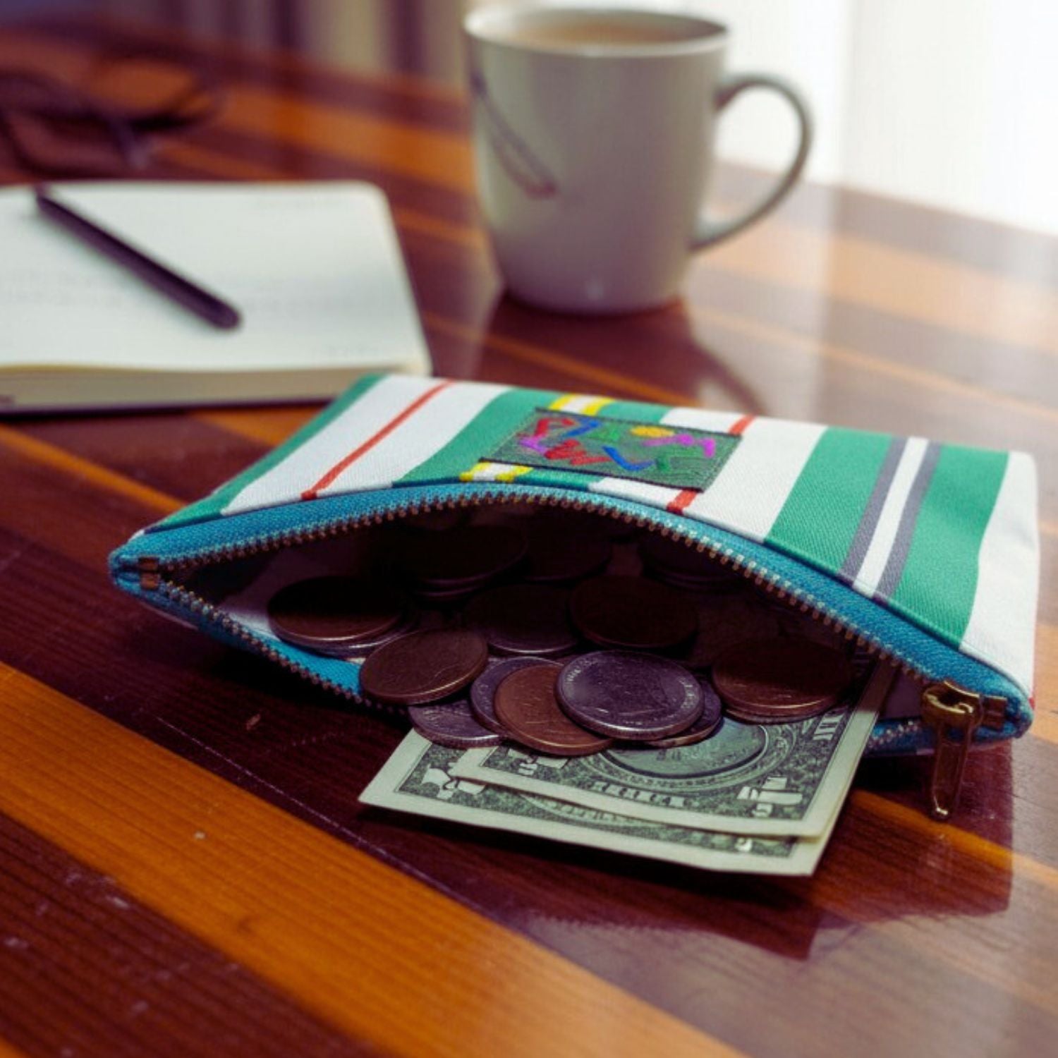 Un monedero de rayas de colores con monedas y un billete de dólar sobre una mesa de madera.