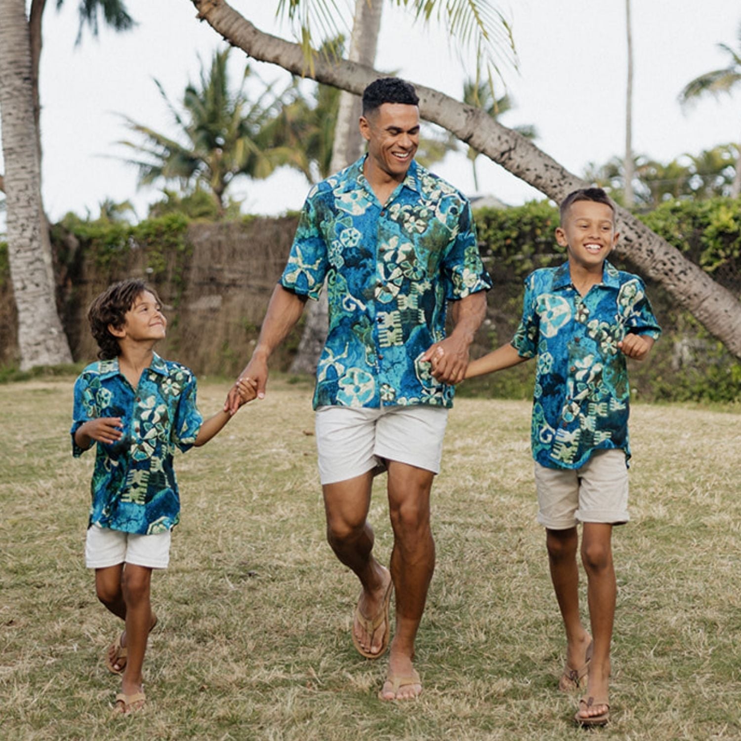 Man and two boys in matching blue floral shirts walking together outdoors.