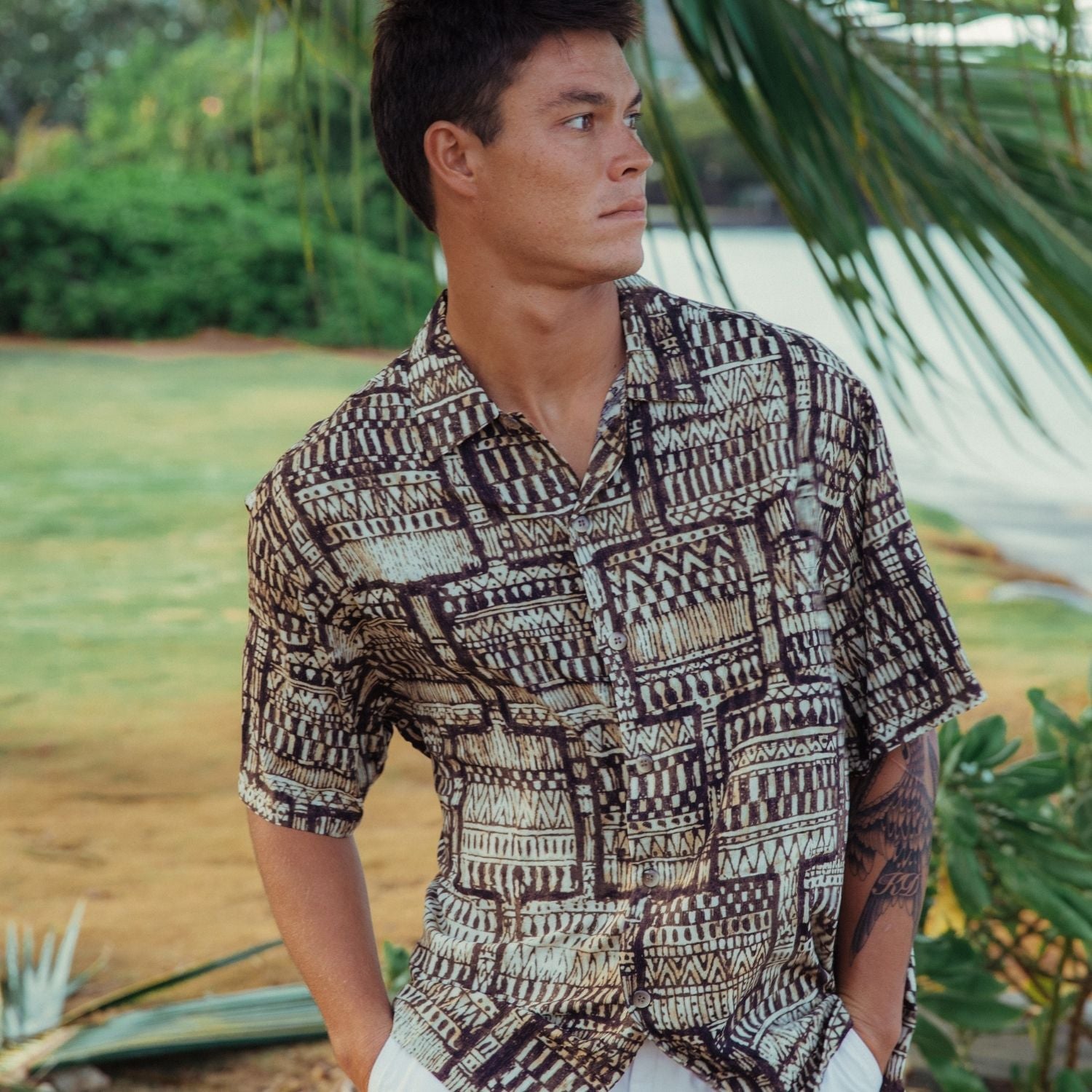 Hombre con camisa estampada en un entorno tropical con plantas.