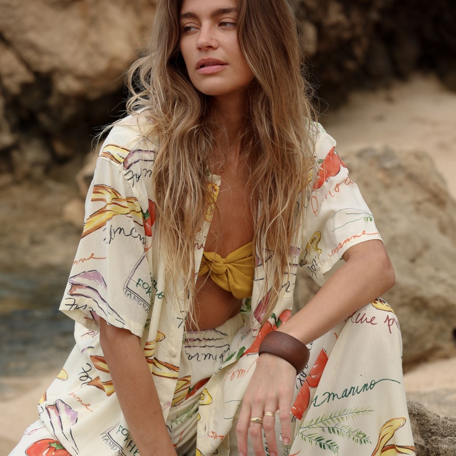 Woman in a colorful outfit sitting on a rocky beach