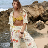 Woman in a patterned outfit standing on a rocky beach.