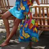 Person wearing a colorful skirt and holding a matching tote bag with fish design outdoors.