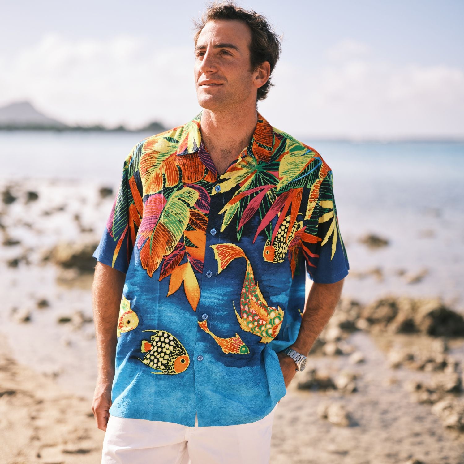 Man wearing a colorful Hawaiian shirt with fish design on a beach