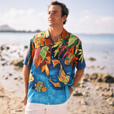 Man wearing a colorful Hawaiian shirt with fish design on a beach