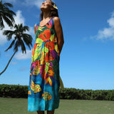 Woman wearing a colorful dress with floral and fish patterns, standing outdoors with palm trees and blue sky in the background.