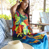 Woman wearing a colorful dress with floral patterns sitting outdoors.