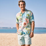 Man wearing a colorful floral shirt and light shorts standing on a beach.