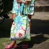 Person wearing a colorful floral dress holding a matching floral bag outdoors.