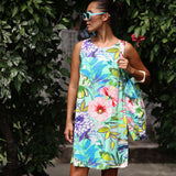 Woman wearing a colorful floral dress and sunglasses standing among greenery.