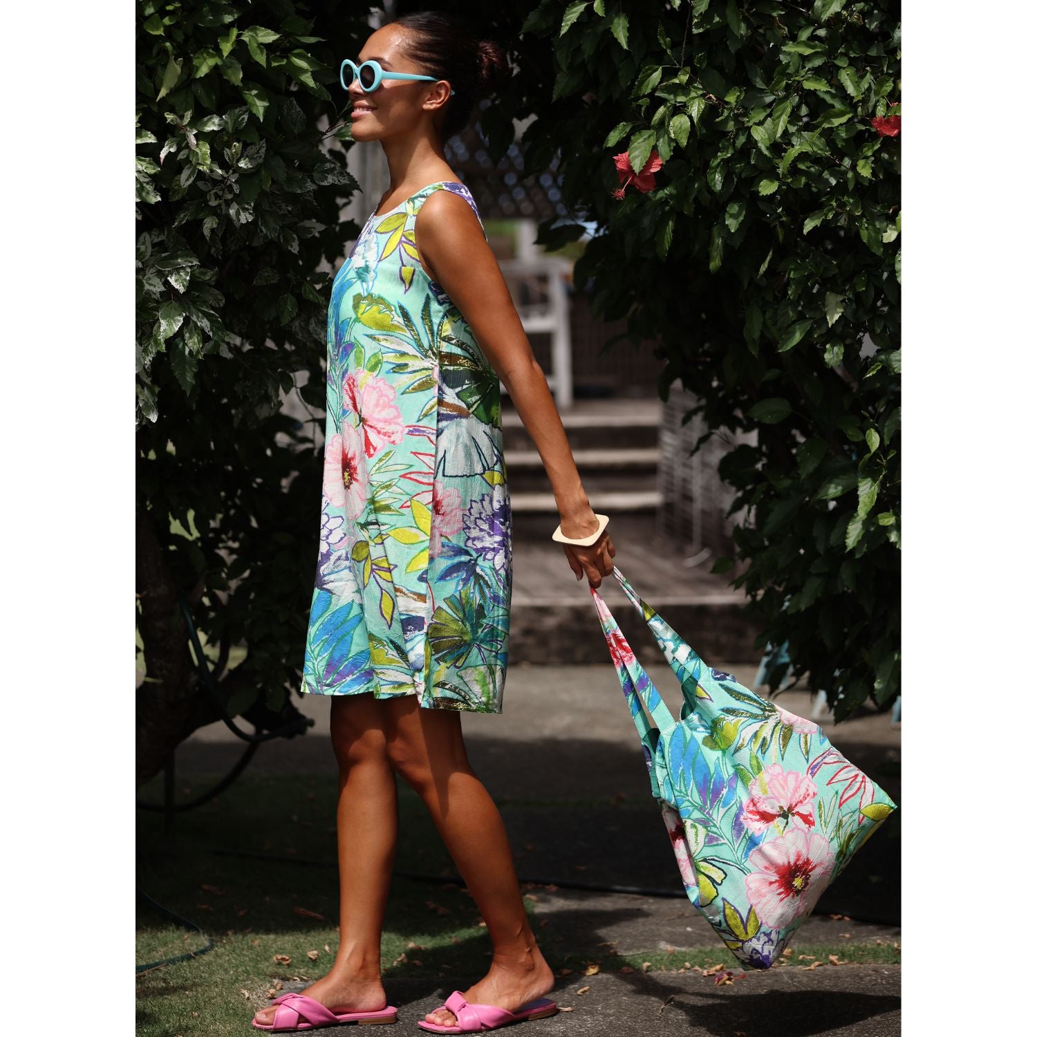 Woman in a floral dress holding a matching bag outdoors.