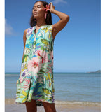 Woman in a colorful floral dress standing on a beach with clear blue sky and ocean.