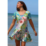 Woman wearing a colorful floral dress standing on a beach.