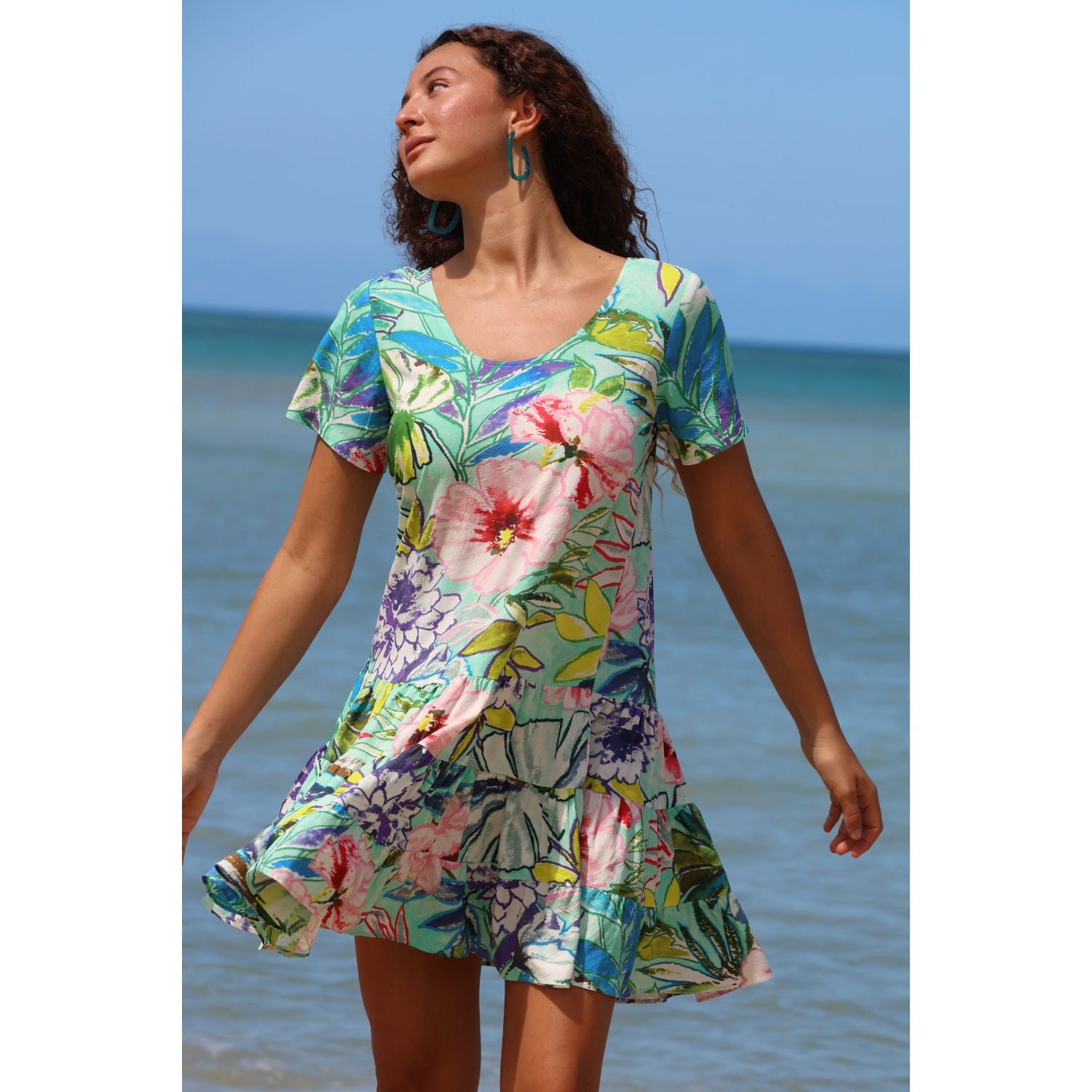 Woman wearing a colorful floral dress standing on a beach.