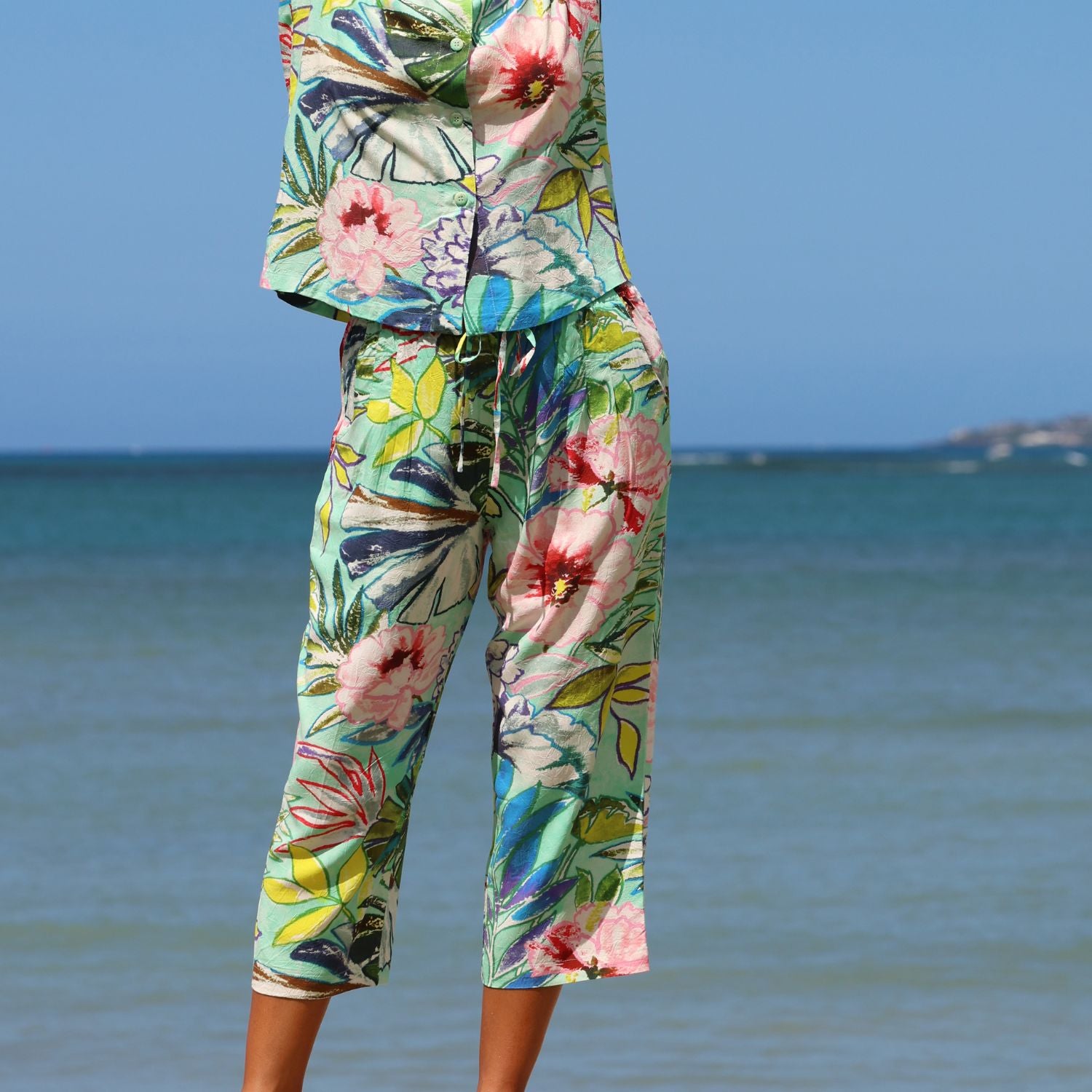 Person wearing a colorful floral outfit standing by the ocean.