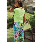 Woman wearing a bright green top and colorful floral pants in an outdoor setting.