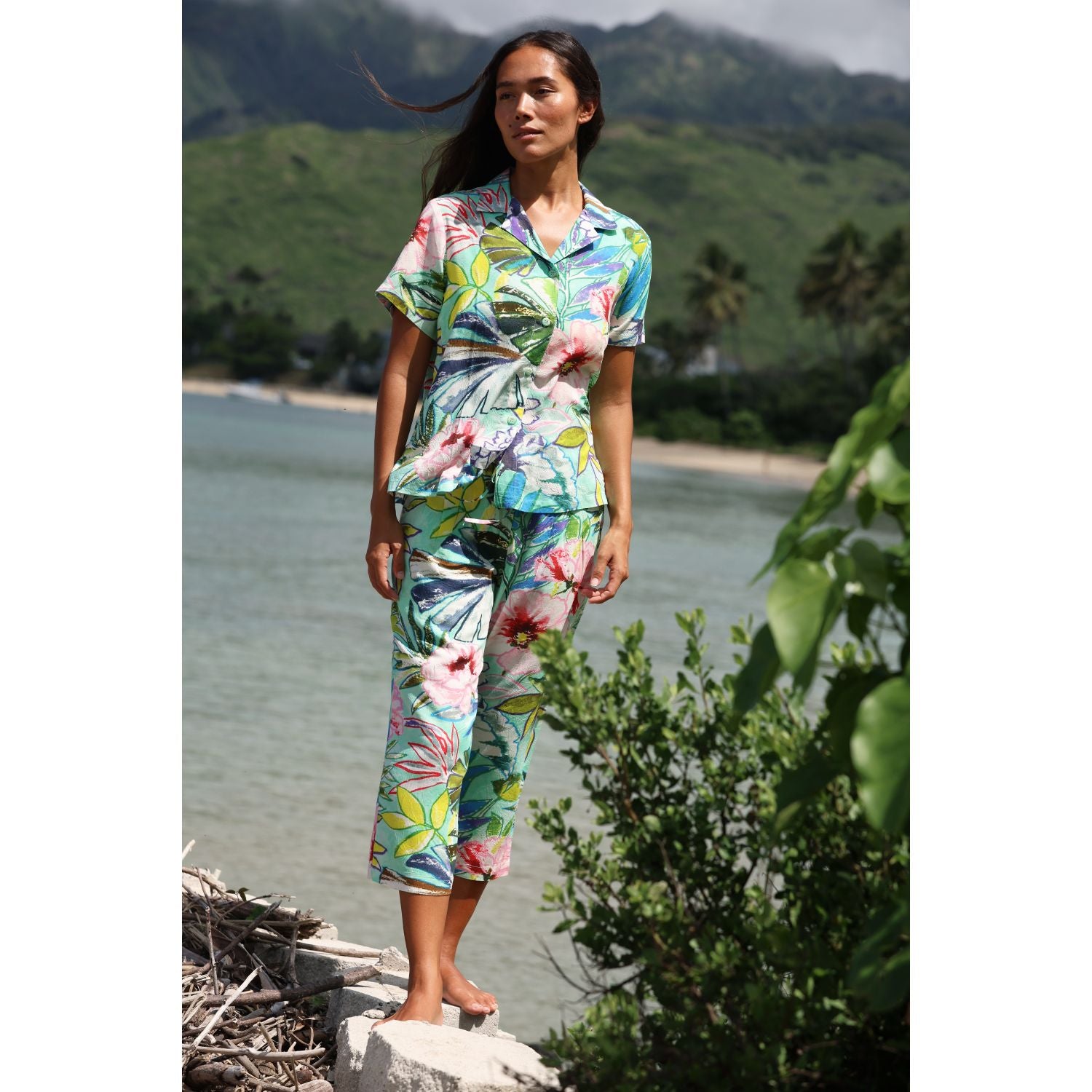 Woman in a floral outfit standing by a body of water with mountains in the background