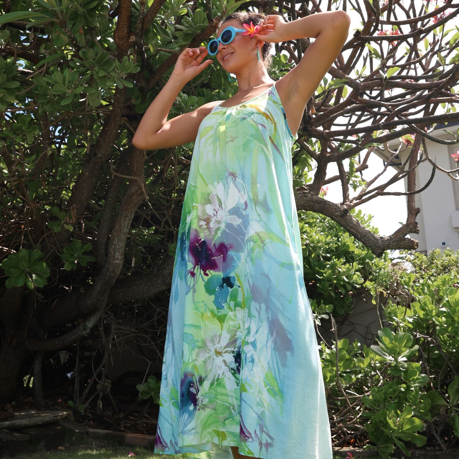 Woman wearing a colorful floral dress standing outdoors with greenery in the background
