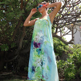 Woman wearing a colorful floral dress standing outdoors with greenery in the background